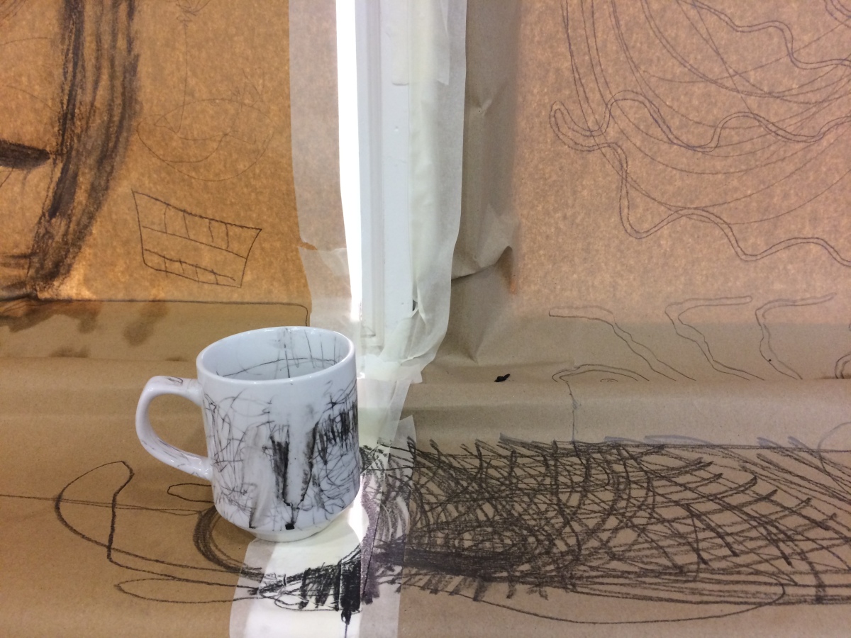 A mug on a windowsill. The wall and window is comepltely covered in brown paper which has been scribbled all over. The mug has also been drawn on the whole picture is covered in doodling lines and marks.